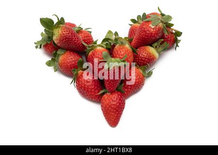 A bunch of whole strawberries with their green leaves, laid out in the shape of a heart. Isolated on white background. Stock Photo