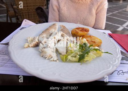 A sea bream fish with roast potatoes and salad. All served on a white plate. Stock Photo