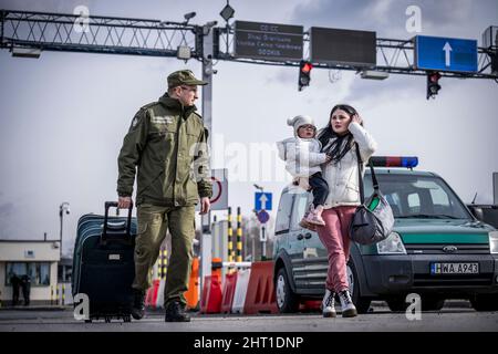 Przemysl, Poland. 26th Feb, 2022. A border guard helps a refugee from Ukraine with her luggage after crossing the border from Shehyni in Ukraine to Medyka in Poland. Many Ukrainians leave the country after military actions by Russia on Ukrainian territory. Credit: Michael Kappeler/dpa/Alamy Live News Stock Photo