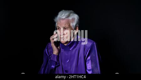 Elderly woman talking on a mobile phone on a black background Stock Photo