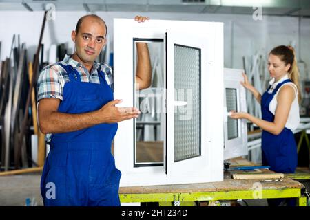 Workman in blue overalls demonstrating pvc window Stock Photo