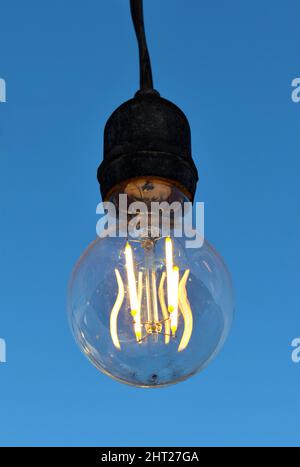 Close-up of a lit light bulb, filaments in the middle of a light bulb, blue background. Stock Photo
