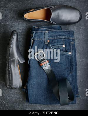 Flat lay mens jeans, moccasins and leather belt, mens fashion, top view, dark gray background Stock Photo