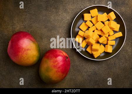 Mango is a tropical fruit. Two whole ripe mangoes and mango cubes in sugar on a dark background with copy space Stock Photo