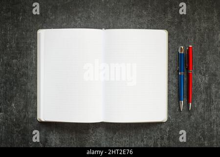 Open blank notebook and 2 colored metallic pens on dark gray background Stock Photo