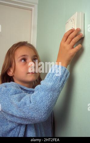 young girl turning down central heating thermostat Stock Photo