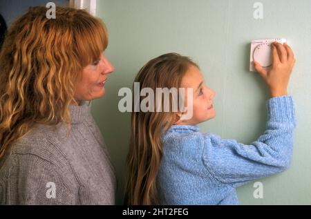 mother with young girl turning down central heating thermostat Stock Photo