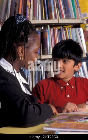 African woman reading with asian boy in library who has special needs Stock Photo