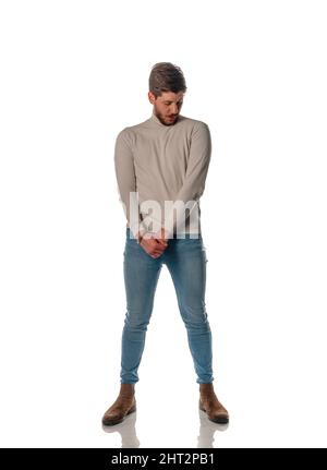 Cool young man dressed in beige pullover posing in modern studio against white background Stock Photo