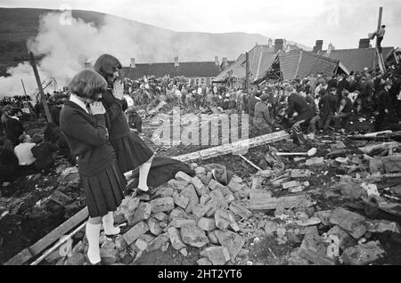 Aberfan - 21st October 1966 Two young school girls prey for the safety of those trapped in the mud, as the rescue effort for survivors at The Pantglas Junior School frantically goes on.  The Aberfan disaster was a catastrophic collapse of a colliery spoil tip in the Welsh village of Aberfan, near Merthyr Tydfil. It was caused by a build-up of water in the accumulated rock and shale, which suddenly started to slide downhill in the form of slurry and engulfed The Pantglas Junior School below, on 21st October 1966, killing 116 children and 28 adults.   The original school site is now a memorial g Stock Photo
