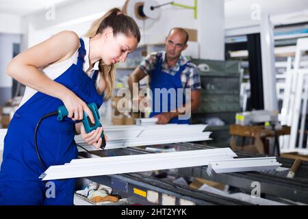 Craftswoman is assembling metal-plastic window using electric drill. Stock Photo