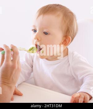 Hes got a good appetite. A cute baby accepting a spoonful of food by his mom. Stock Photo