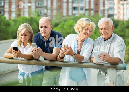 Positive mature couples holding gadgets in park Stock Photo