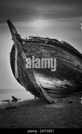 Vertical, grayscale shot of a rustic, wooden boat on a beach Stock Photo
