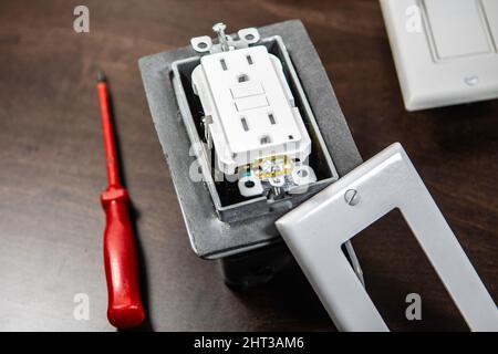 A tested electrical outlet lies on the table before being installed in a junction box on the wall. Stock Photo