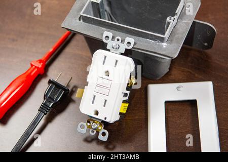 A tested electrical outlet lies on the table before being installed in a junction box on the wall. Stock Photo