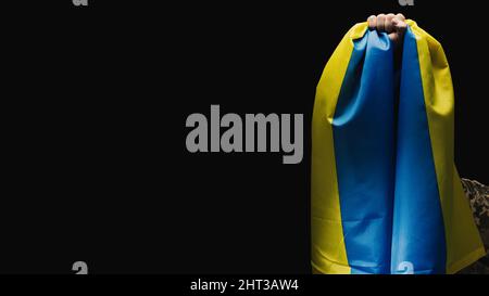 Ukrainian soldier holds a flag of the independent state of Ukraine. Steadfastness and courage of the people in the fight against the invaders. Unbroke Stock Photo