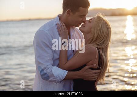 Man and woman kissing while standing on beach on background of sunset Stock Photo