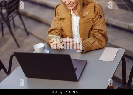 Lady dressed in leather trench coat using smartphone in street cafe Stock Photo