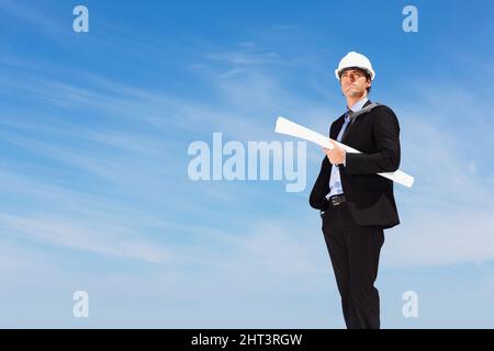 An architect with blueprints standing against clear sky. Business blueprint - An architect with papers standing against clear sky. Stock Photo