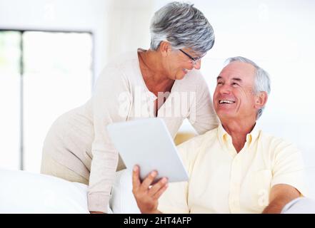 Cheerful mature couple using tablet PC. Cheerful mature couple smiling while using tablet PC at home. Stock Photo