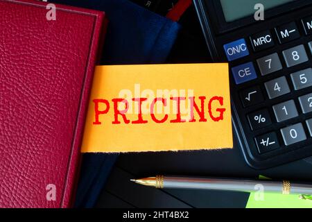 On the table there are reports, a pen, a calculator and a white card with the text PRICING. Stock Photo