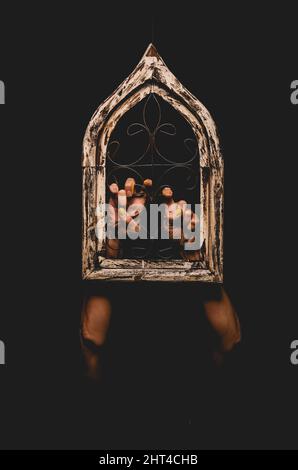 Vertical shot of dramatic hands holding on a window isolated on black background Stock Photo