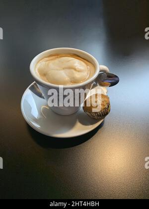 A cup of coffee with a lot of foam and milk and a mini cupcake to start the day with energy Stock Photo