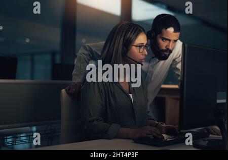 Together we can get it done. Shot of two call centre agents working together in an office at night. Stock Photo