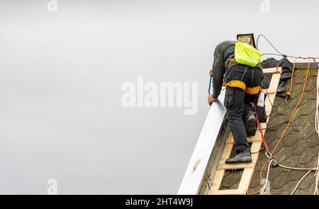 A man works on the roof repair, installs sheet metal on top of the gable wall Stock Photo