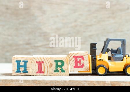 Toy forklift hold letter block e in word hire on wood background Stock Photo