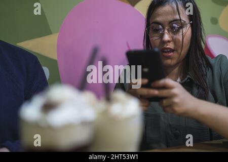 Woman using her smartphone with a blurry milkshake foreground Stock Photo