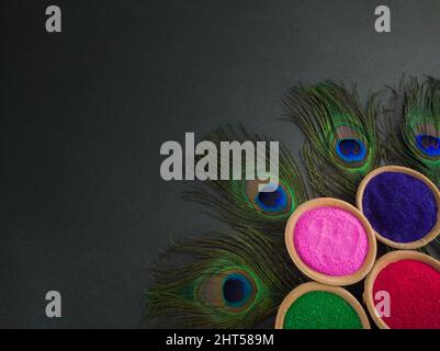 colorful powders for holi on clay pots on occasion of indian festival of colors. happy holi theme shot against black background with peacock feathers. Stock Photo