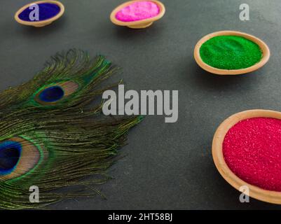 colorful powders for holi on clay pots on occasion of indian festival of colors. happy holi theme shot against black background with peacock feathers. Stock Photo