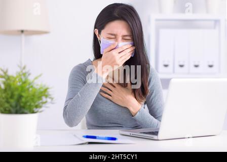 Stressed young  woman wearing medical face mask and working at home office Stock Photo