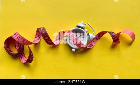 Measuring tap on alarm clock and yellow paper. Weight loss concept Stock Photo