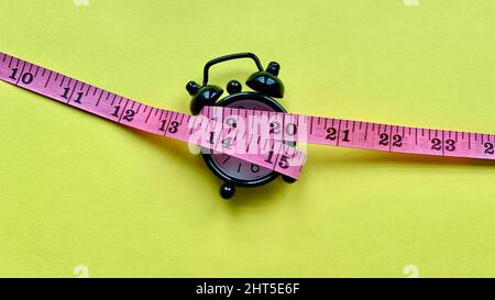 Measuring tap on alarm clock and yellow paper. Weight loss concept Stock Photo