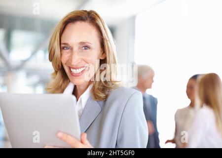 Business woman using electronic tablet. Portrait of mature business woman working on electronic tablet with executives in background. Stock Photo