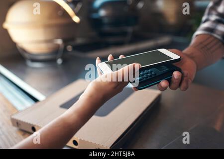 Paying the modern way. Cropped shot of an unrecognizable woman standing and using her cellphone to pay for her meal at a restaurant. Stock Photo