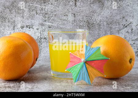 Close-up shot of an orange soda in a glass tumbler and three oranges on a gray table Stock Photo