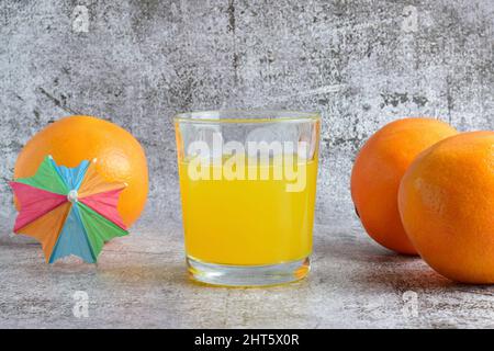 Close-up shot of an orange soda in a glass tumbler and three oranges on a gray table Stock Photo