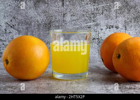Close-up shot of an orange soda in a glass tumbler and three oranges on a gray table Stock Photo