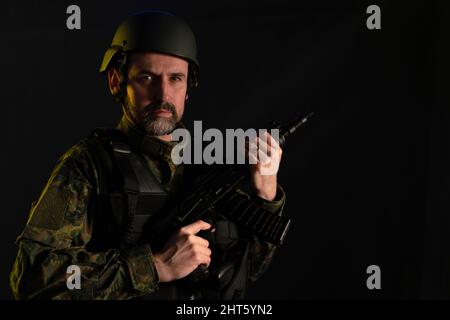 Soldier in military uniform and helmet with weapon looking at camera on black background. Stock Photo