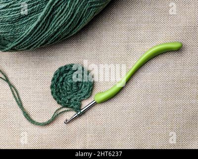 Green yarn thread with crochet hooks for knitting and hobbies on gray background from fabric. Top view. Copy space. Selective focus. Stock Photo