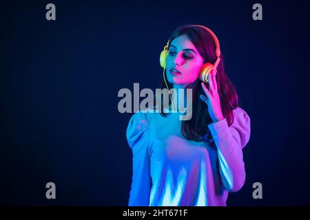 Young caucasian woman wearing yellow headphones illuminated with neon lights on black background Stock Photo