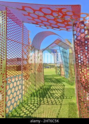 Vertical shot of a maze made of colorful mesh panels with a green grass path under blue skies Stock Photo
