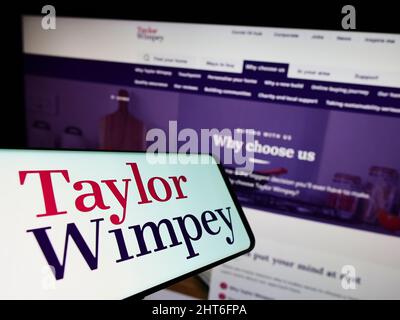 Smartphone with logo of British housebuilding company Taylor Wimpey plc on screen in front of website. Focus on center-right of phone display. Stock Photo
