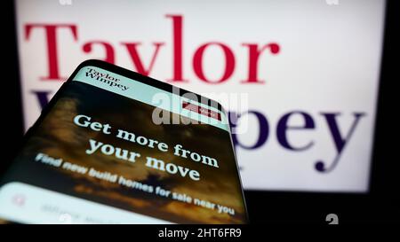 Mobile phone with webpage of British housebuilding company Taylor Wimpey plc on screen in front of logo. Focus on top-left of phone display. Stock Photo