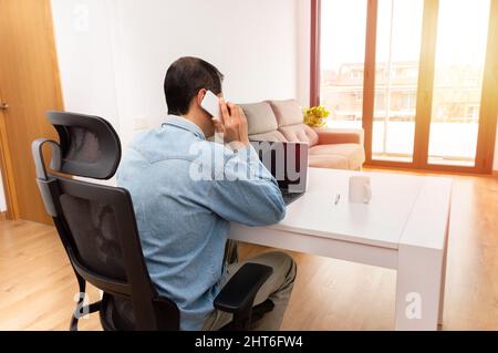 Rear view of a young businessman sitting alone in his home office and talking on his cellphone Stock Photo