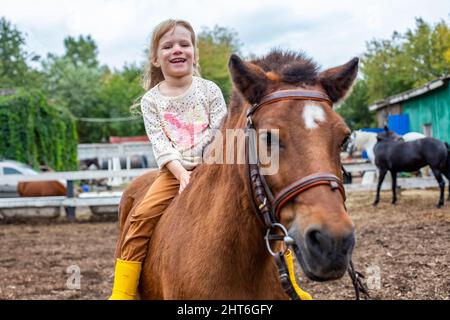 happy little girl riding pony horse bareback and laugh Stock Photo